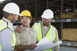 Multi-ethnic workers (20s, 30s) with hardhats and safety vests, in lumber yard.