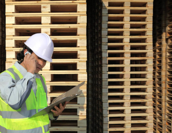 Employee in hardhat next to piles of wood pallets