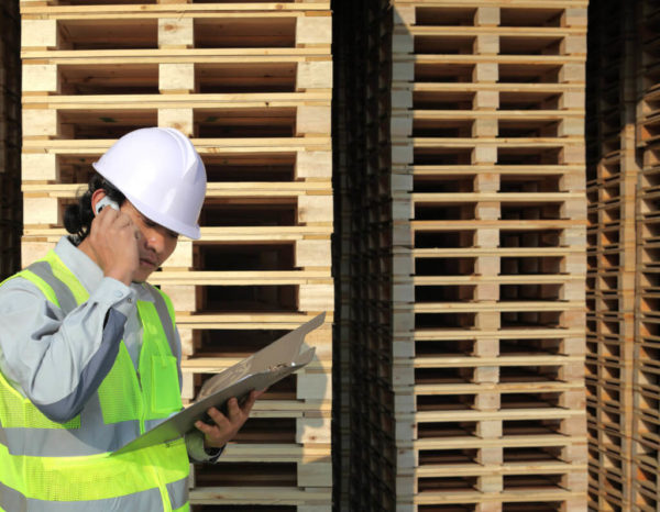 Employee in hardhat next to piles of wood pallets